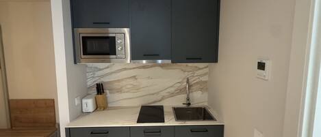 A compact kitchen with dark cabinets, a microwave, a sink, and a marble backsplash.