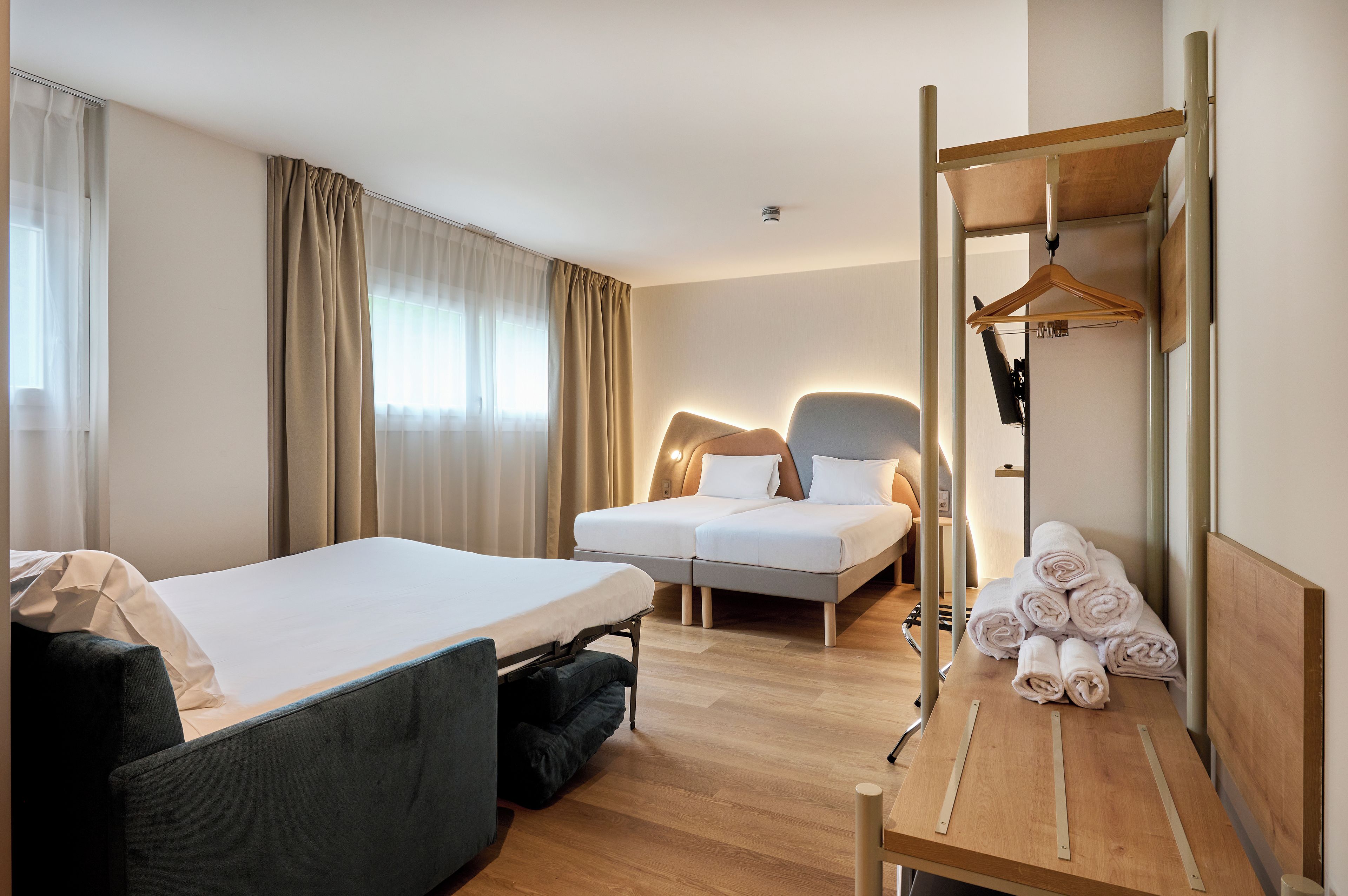A hotel room with a bed, a sofa, a desk, and a mirror.