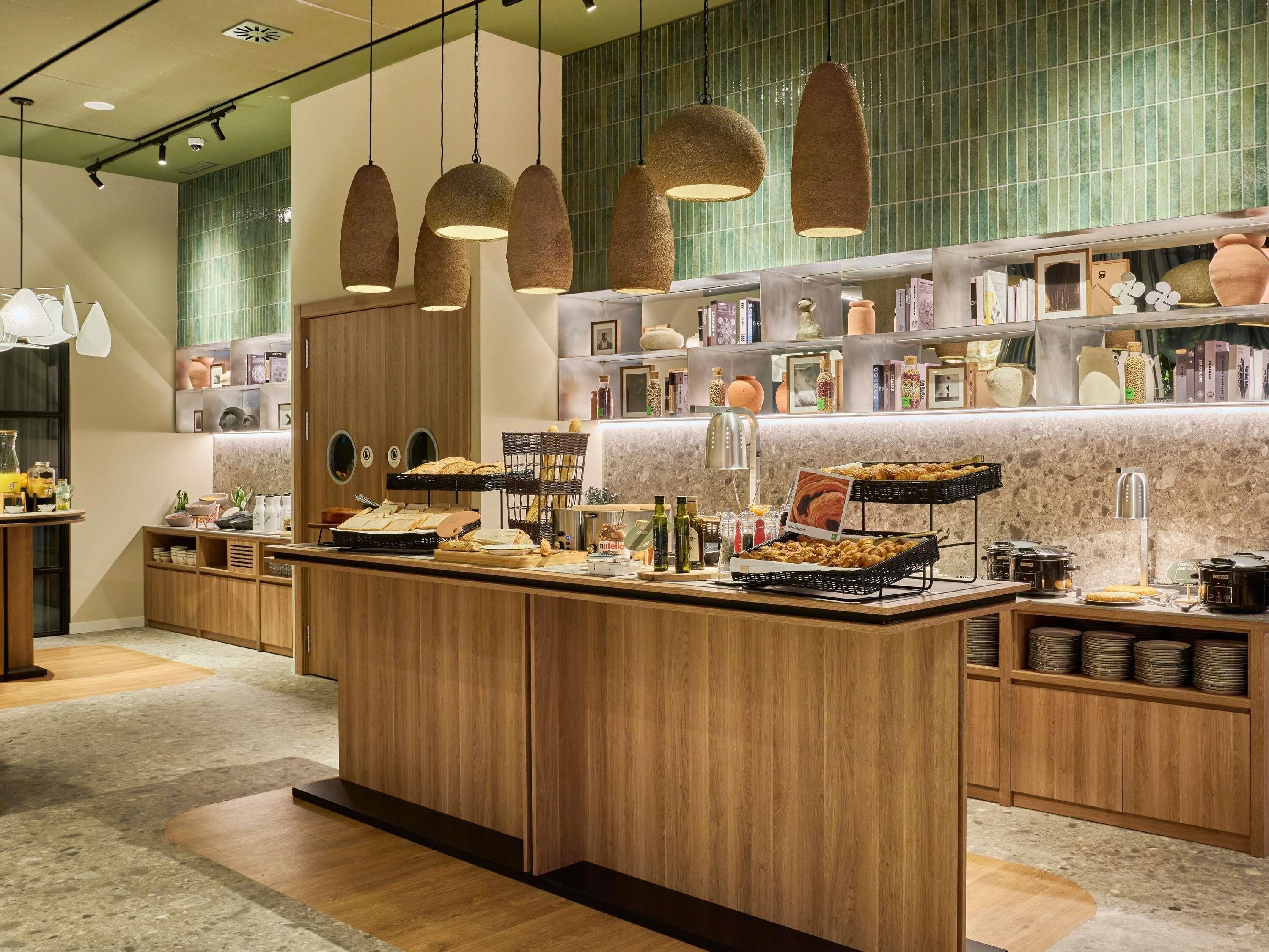 Un espace cuisine moderne avec des meubles en bois, un îlot central où sont disposés des aliments, des luminaires suspendus et un dosseret de carrelage vert.