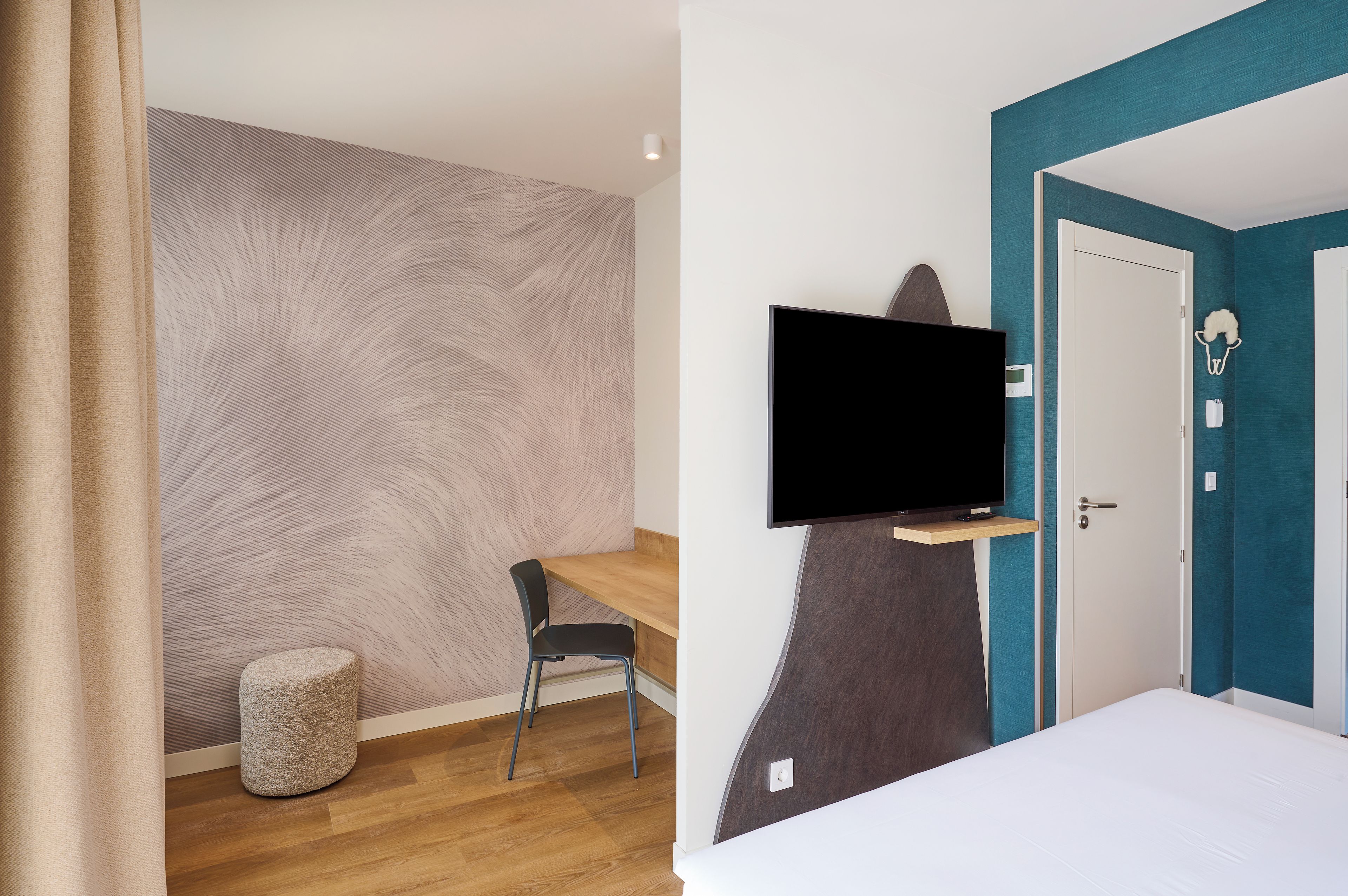 Una habitación de hotel con un escritorio de madera, un televisor montado en la pared, un taburete pequeño y una cama.