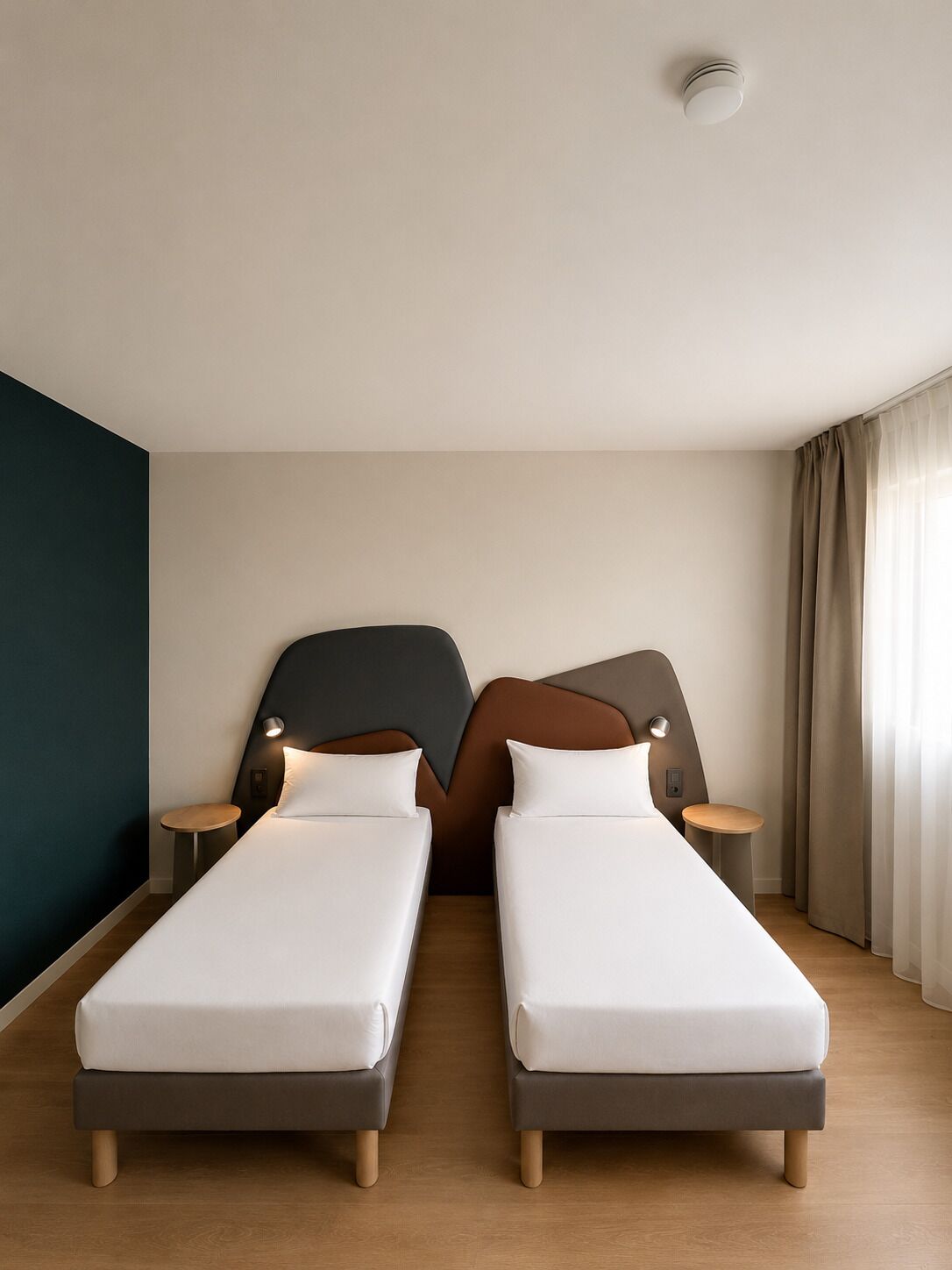 Hotellihuone, jossa on kaksi erillistä sänkyä, tumma tehosteseinä, kattovalaisin ja ikkuna, jossa on verhot.