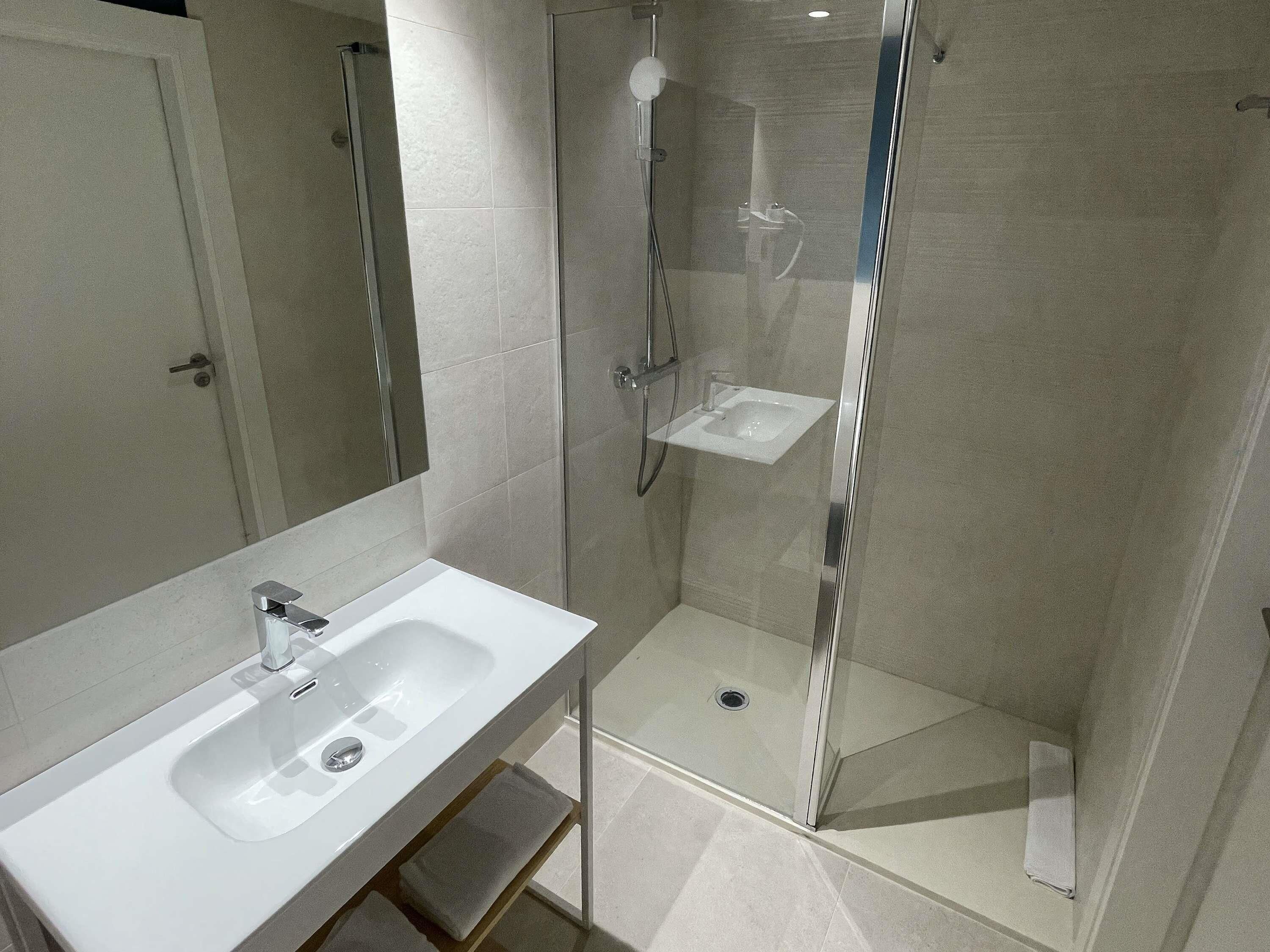 A modern bathroom with a glass-enclosed shower, a white sink, and a mirror.