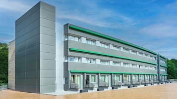 Un edificio moderno con techo plano, múltiples ventanales y un detalle verde en los pisos superiores.