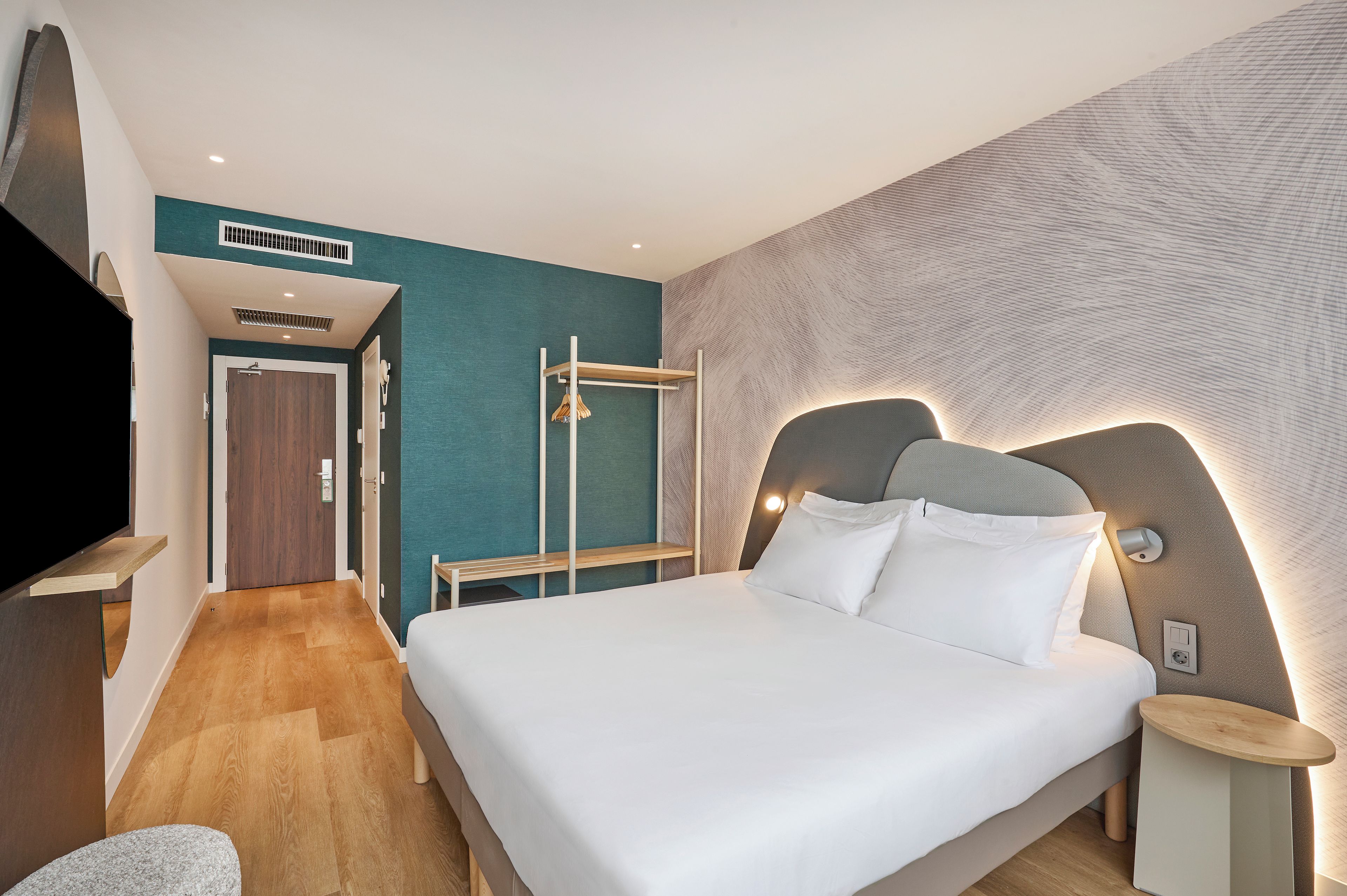 A hotel room with a bed, bedside table, and a headboard with integrated lighting.