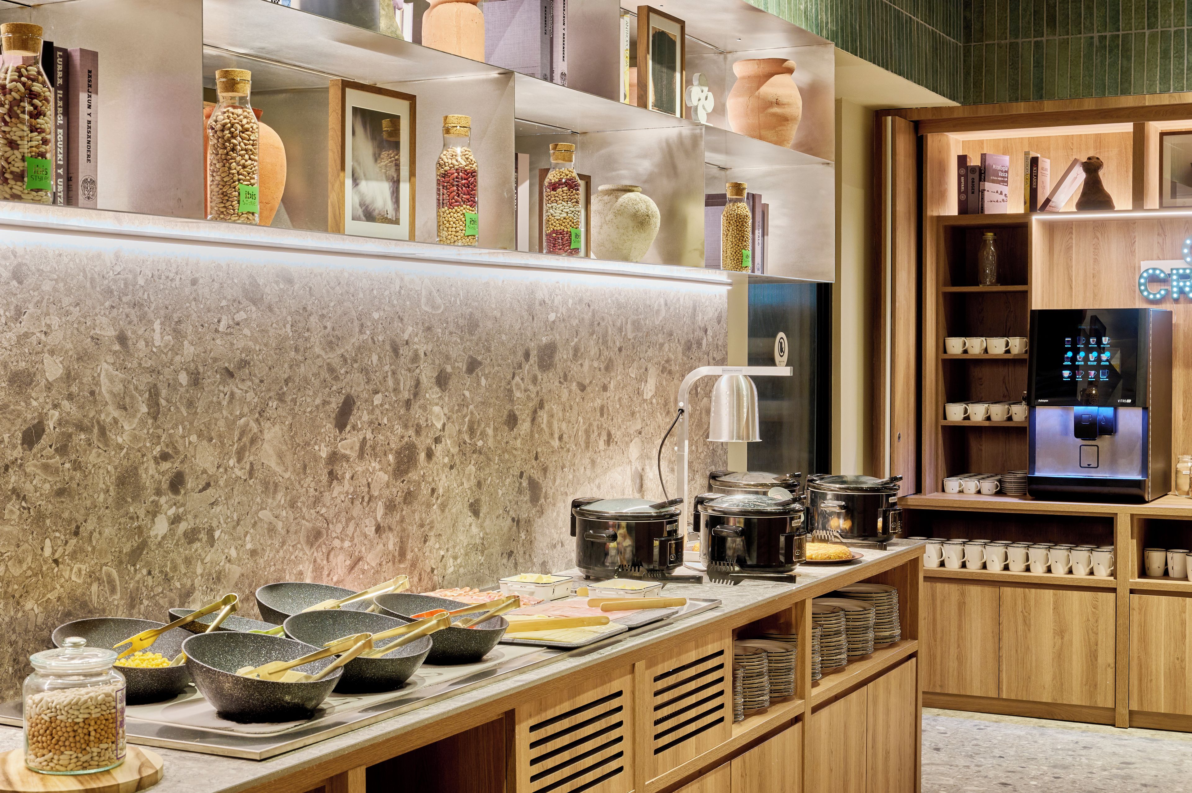 Un área de cocina con cafetera, utensilios de cocina y estantes con frascos y libros.