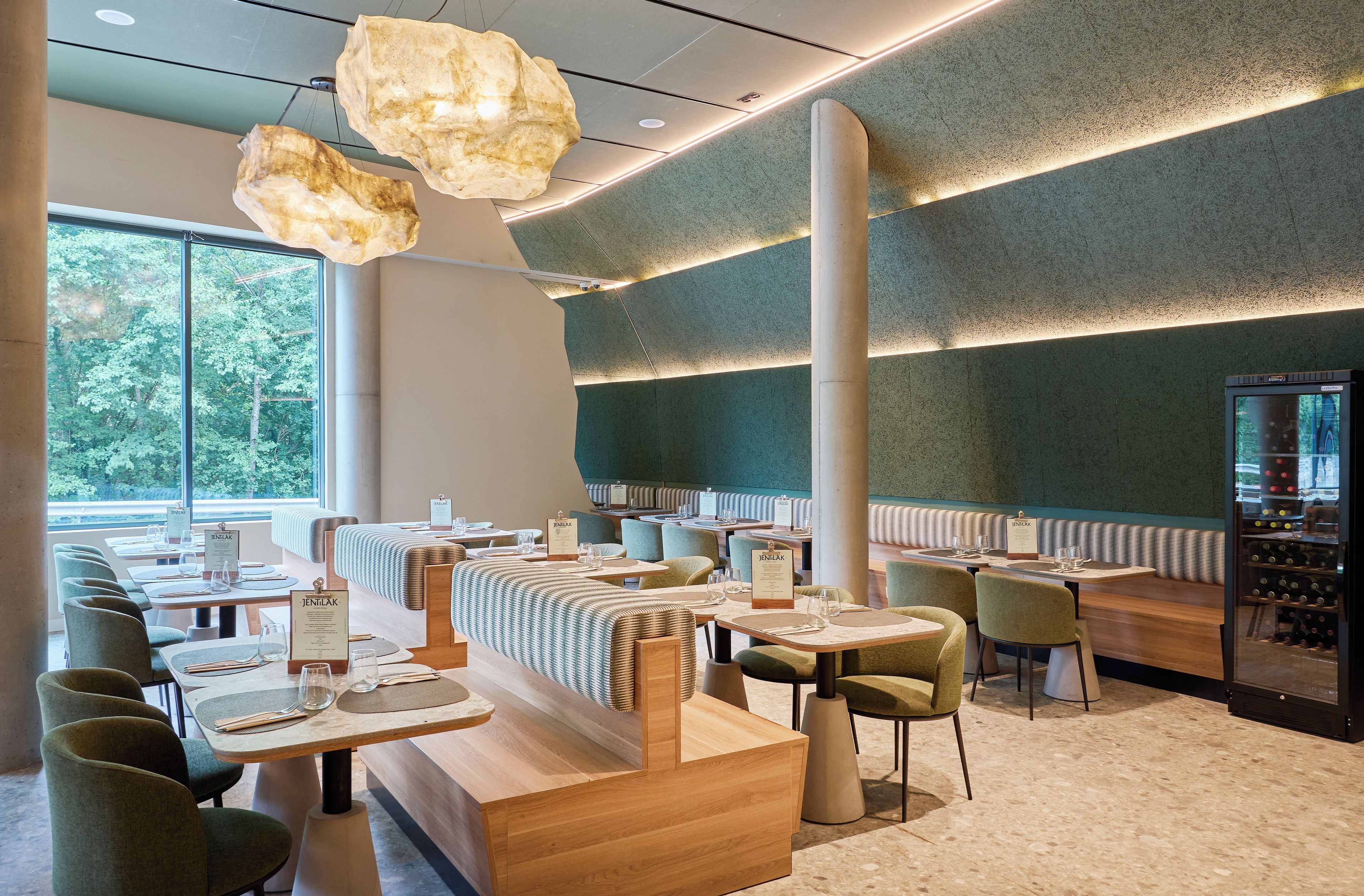 Interior de un restaurante con cabinas, mesas y una estantería para vinos.