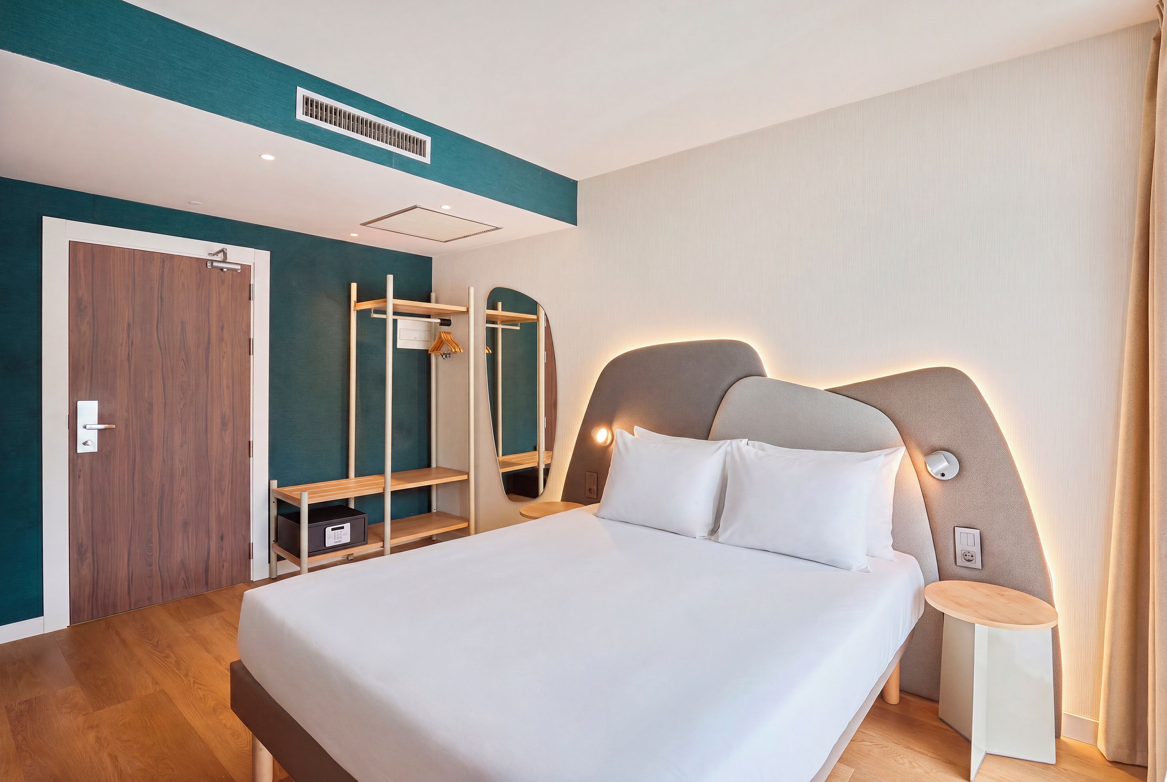 Una camera d'albergo moderna con un letto grande, un comodino, un armadio e uno specchio.