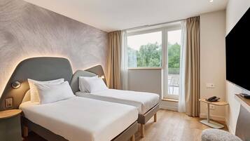 Une chambre d’hôtel avec deux lits, une télévision, un bureau avec un téléphone et une fenêtre avec des rideaux.