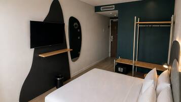 Habitación de hotel moderna con una cama, un televisor de pantalla plana, un adorno con forma de tabla de surf y un sofá cama.