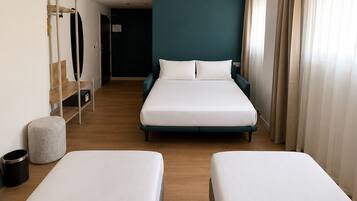 Une chambre d’hôtel avec deux lits, un bureau, une chaise, un petit tabouret, une poubelle et une porte donnant sur une autre pièce.