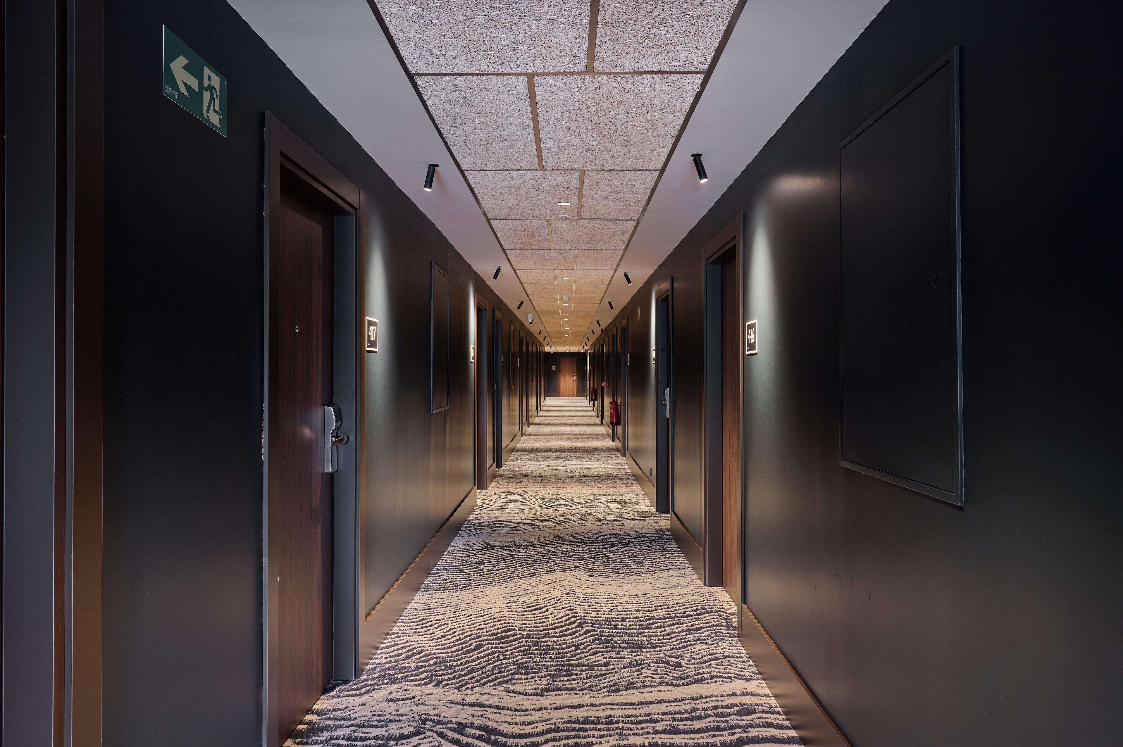 A long, narrow hallway with doors on both sides, a patterned carpet, and recessed lighting on the ceiling.