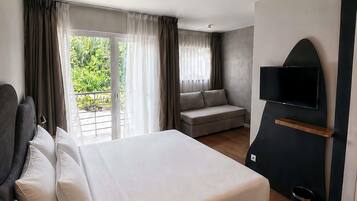 Ein Hotelzimmer mit Bett, einer Couch, einem Fernseher und einem Balkon mit Vorhängen.