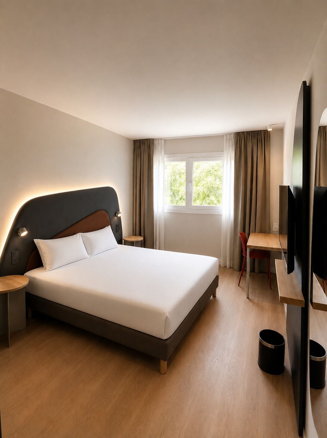 Ett modernt hotellrum med en stor säng, ett skrivbord, en stol, en tv och ett fönster med gardiner.