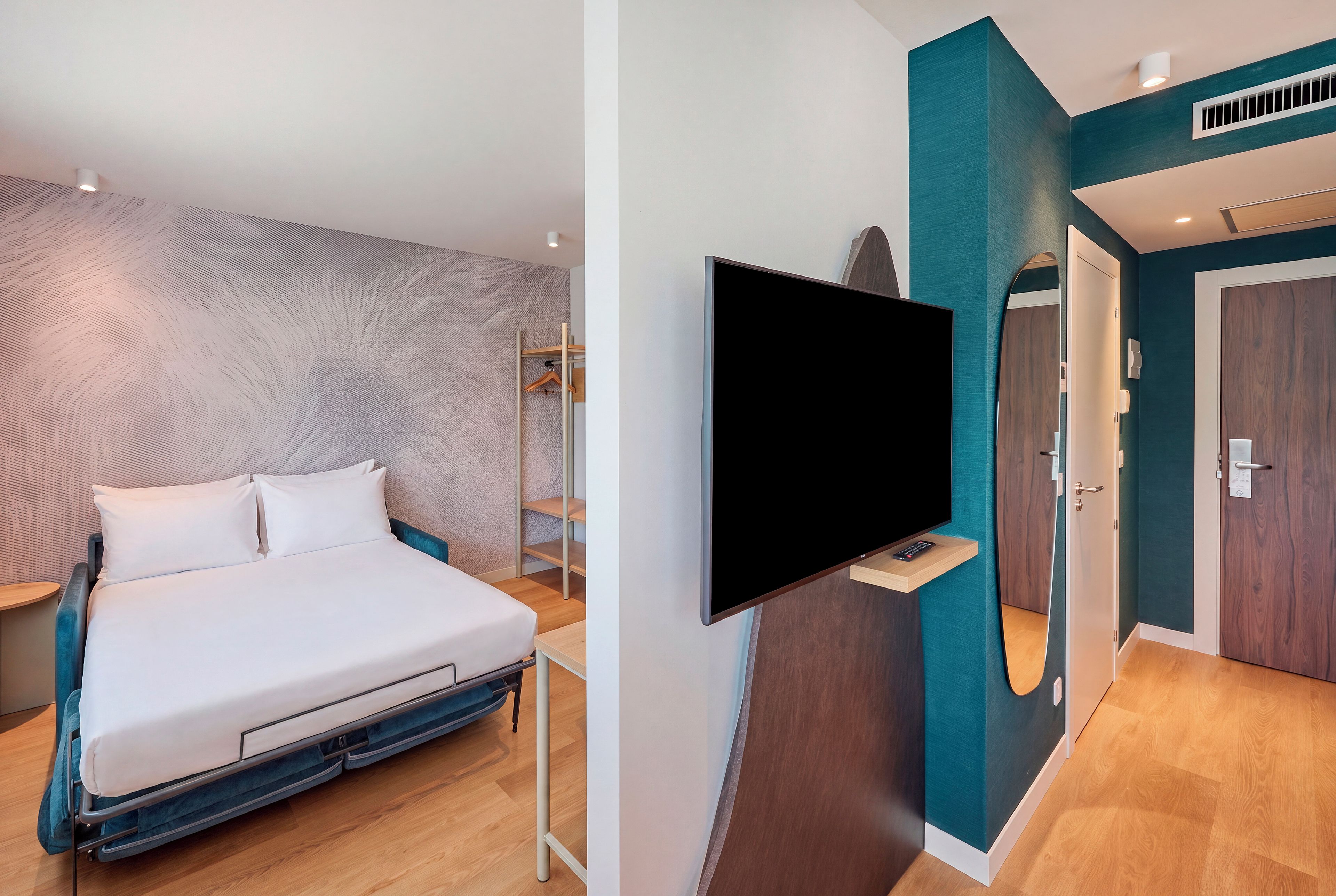 Une chambre d’hôtel moderne équipée d’un lit, d’un téléviseur fixé au mur, d’une armoire et d’un miroir.