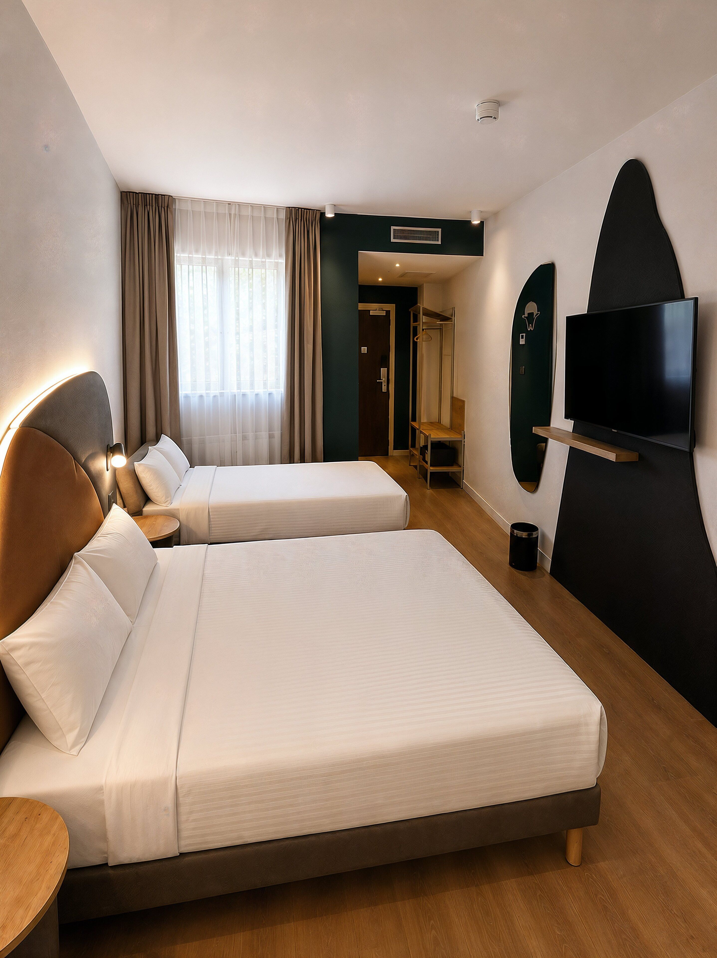A hotel room with two beds, a TV, a coat rack, and a bathroom door.