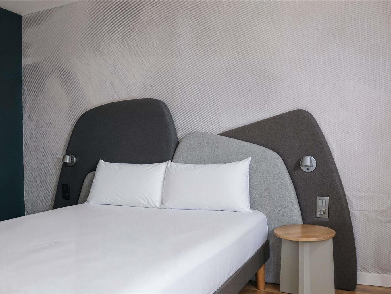 A modern bed with a grey headboard, white bedding, and a small wooden side table.