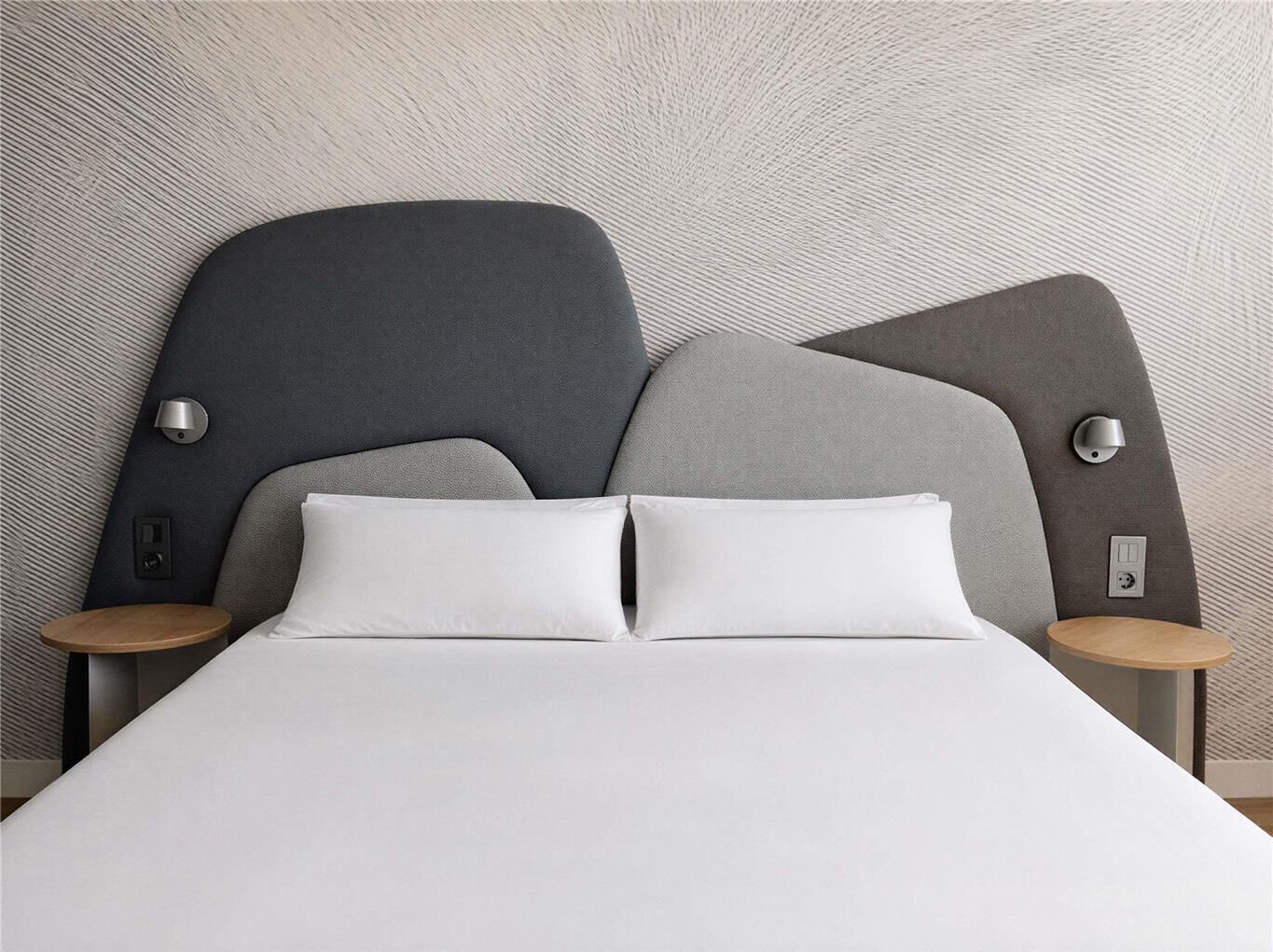A modern bed with a unique headboard design, two bedside tables, and a textured wall.