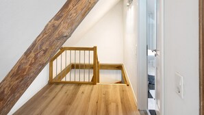 Eine Holztreppe mit Metallgeländer führt zu einem Raum mit weißen Wänden und einer Tür.