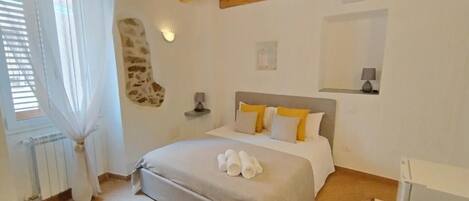 A bedroom with a bed, a stone wall, a bedside table, a lamp, and a window with curtains.