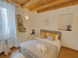 Une chambre à coucher avec un lit, un mur en pierre, un miroir et une fenêtre avec des rideaux.