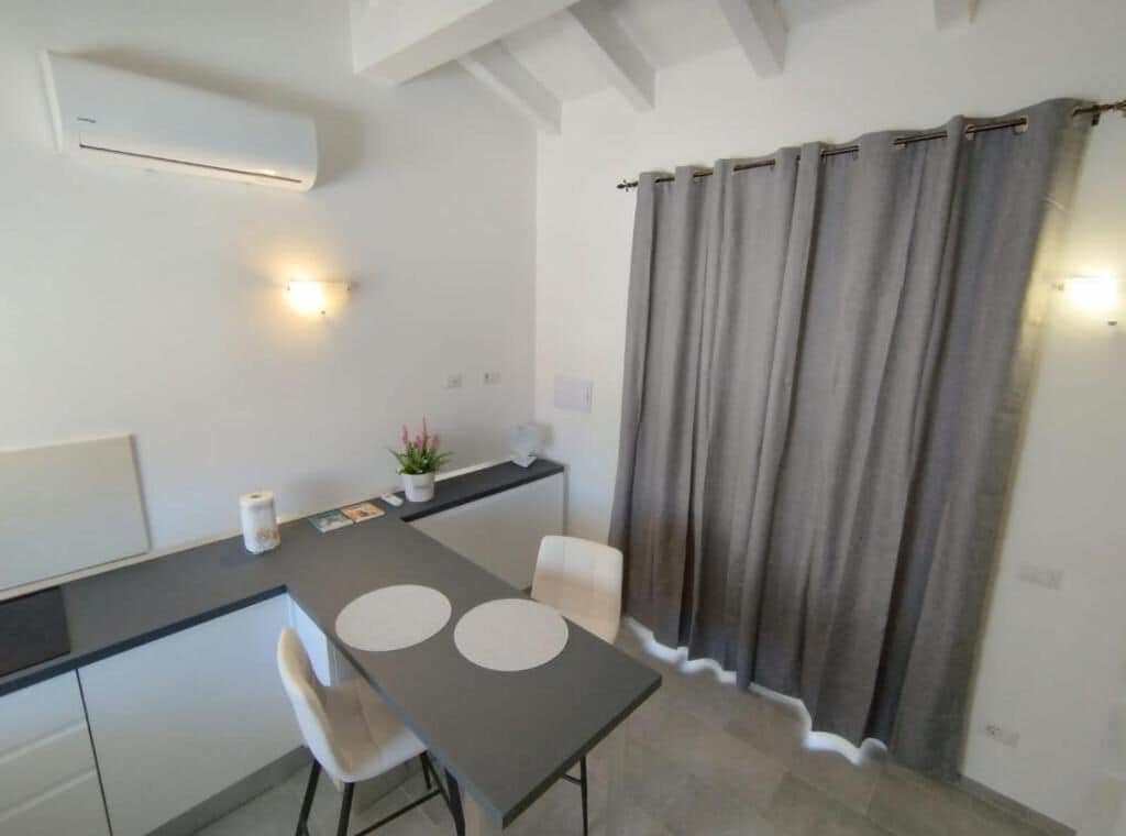 Una cocina moderna con una mesa de comedor, sillas, una pequeña barra y una cortina gris.