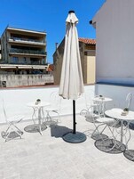 Une terrasse extérieure avec une table et des chaises, un parasol blanc et un bâtiment en arrière-plan.