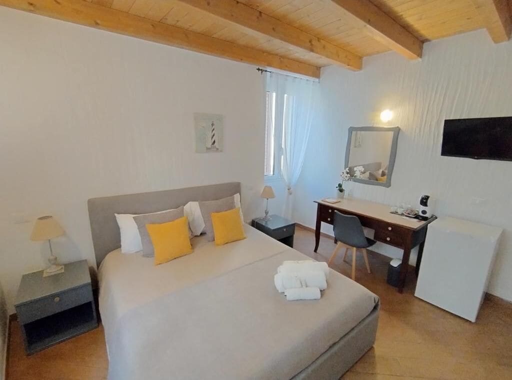A bedroom with a bed, bedside table, desk, chair, and a small refrigerator.