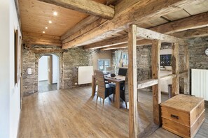 A rustic interior with exposed wooden beams, stone walls, a wooden dining table with chairs, and a small wooden chest. - Apartment 'Kornboden' with Shared Terrace, Shared Garden and Wi-Fi (Neuenrade)