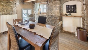 A rustic dining area with a wooden table, chairs, a stone wall, a window with a view, and a decorative wall piece. - Apartment 'Kornboden' with Shared Terrace, Shared Garden and Wi-Fi (Neuenrade)