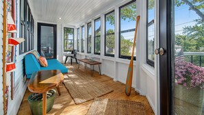 Un solárium con un sofá azul, suelo de madera, ventanas grandes y un bate de béisbol apoyado contra la pared.