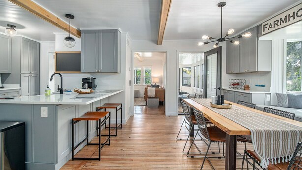 Una cocina moderna con una isla central, taburetes de bar y un comedor con una mesa larga y sillas.