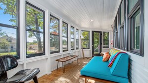 Un solárium con ventanas amplias, un sofá azul, un banco de madera y una silla negra.
