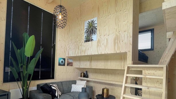 Un interno moderno con un divano grigio, un piccolo tavolo rotondo, una lampada a sospensione e una scala in legno.