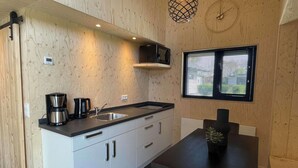 Una cucina compatta con lavandino, fornello e macchina da caffè, un tavolo da pranzo con sedie e una finestra con tende.
