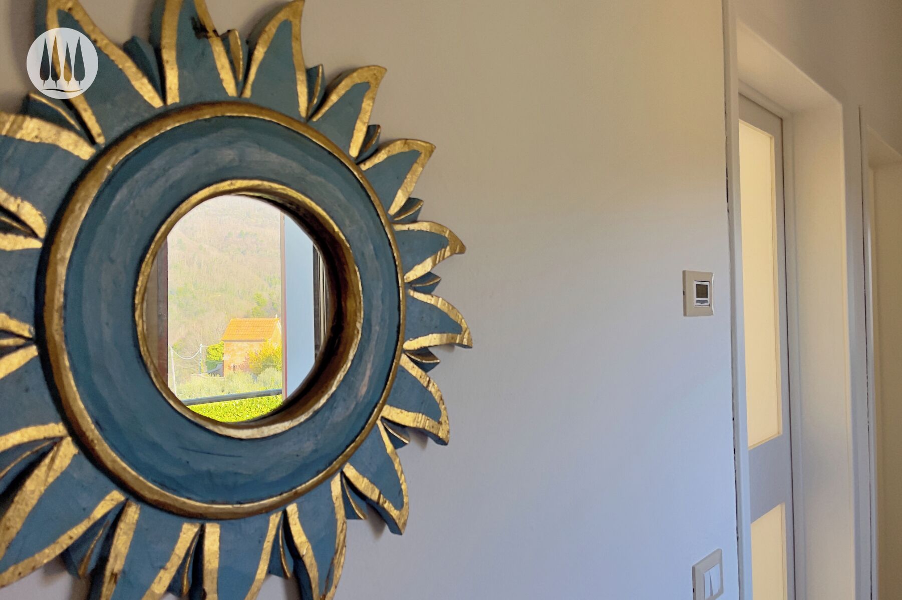 Una habitación con un espejo grande y circular con diseño de rayos de sol en la pared, una puerta y un enchufe eléctrico pequeño.