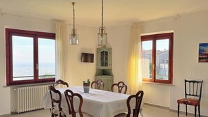 Comedor con una mesa dispuesta para seis personas, dos lámparas colgantes, un radiador, un televisor y vistas de la ciudad a través de ventanas amplias.
