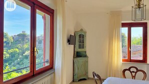 Un dormitorio con una ventana grande, una silla de madera, un armario pequeño y un radiador.