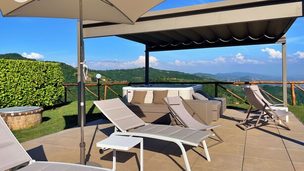 Un patio exterior con sillones, una mesa y un jacuzzi, con vistas a un paisaje montañoso.