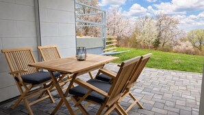 A patio with a wooden table and chairs, a metal railing, and a view of cherry blossoms.
