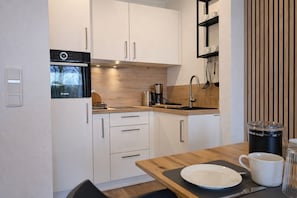 Una cocina moderna con armarios blancos, horno Bosch, cafetera y encimera de madera.
