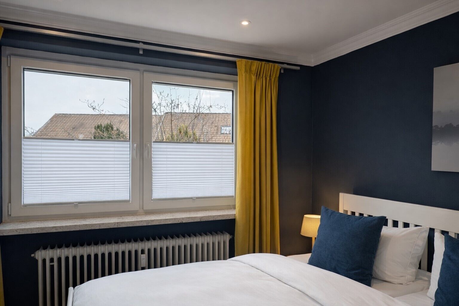 Una camera d'albergo con un letto, una finestra con persiane, un termosifone e un quadro appeso al muro.