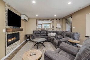 A living room with a sectional sofa, a fireplace, a TV, and a large mirror. - Soaring Eagle: Main house+Bunkhouse: Lakefront (Boyne City)