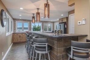 A modern kitchen with a central island, bar stools, pendant lighting, and large windows. - Soaring Eagle: Main house+Bunkhouse: Lakefront (Boyne City)