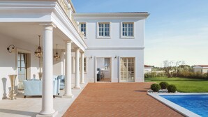 Un edificio blanco con columnas, piscina y jardín.