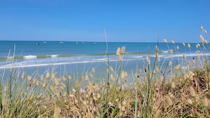 A beach with waves, boats, and tall grass in the foreground.