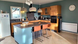 A modern kitchen with a central island, pendant lights, wooden cabinets, and a built-in oven.