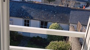 A view through a window with a clear sky, a stone building, and a tree. - Le Picoteu' (Saint-Vaast-la-Hougue)