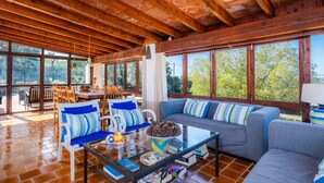 Una habitación amplia con vigas de madera, ventanas grandes, un sofá, sillas y un comedor.