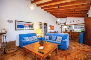 Ein Wohnzimmer mit einem blauen Sofa, einem Holztisch und einer Küche im Hintergrund.