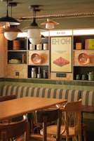 Interior de restaurante con banco de madera, mesas y estantes con utensilios de cocina.